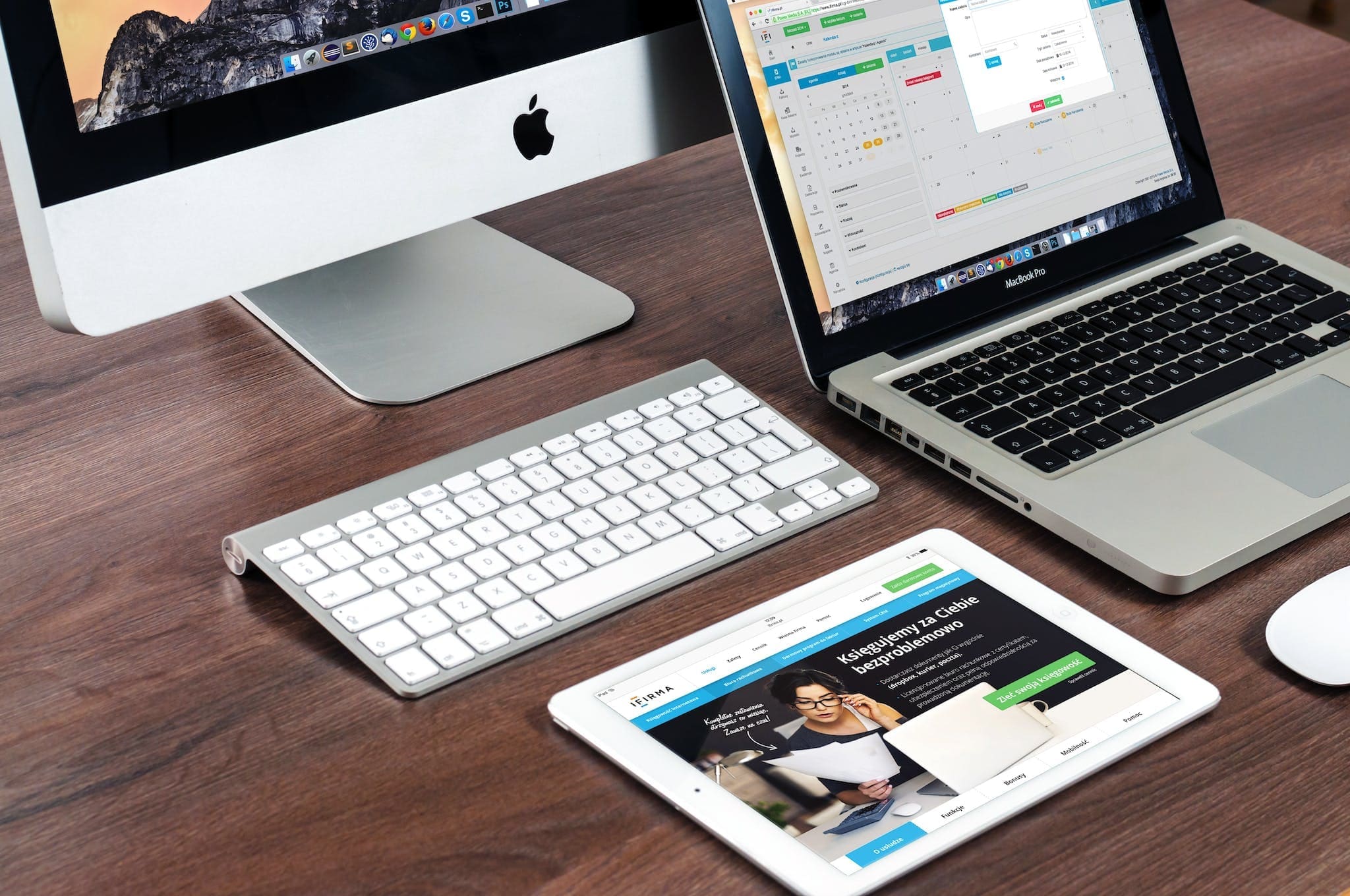A desk with devices with different screen sizes. A tablet, a desktop computer and a laptop